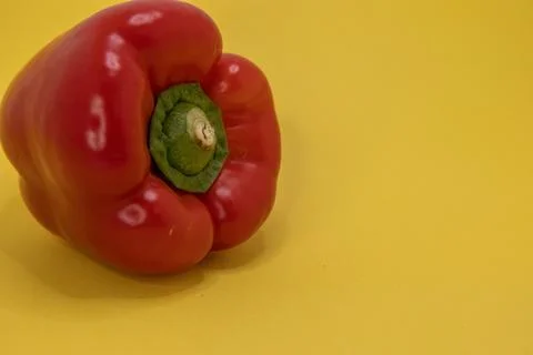 A single red bell pepper sits on a bright yellow background. Stock Photos