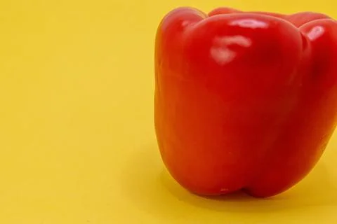 A single red bell pepper sits on a bright yellow background. Fotos de archivo
