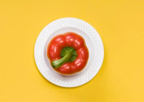Single red bell pepper on white plate  on yellow background Stock Photos