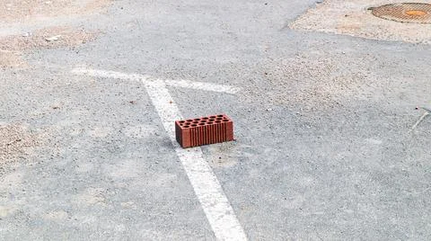 A single red brick rests on a dirty asphalt surface marked with faded white.. Stock Photos
