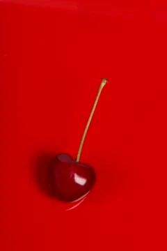 Single red cherry with stem on a red background in a vertical image Stock Photos
