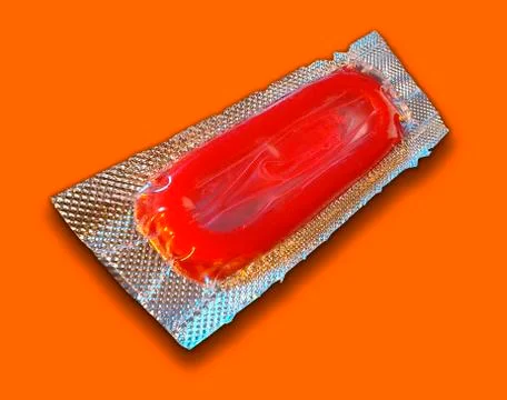 SINGLE RED CONDOM IN FOIL WRAPPER ON ORANGE BACKGROUND Stock Photos