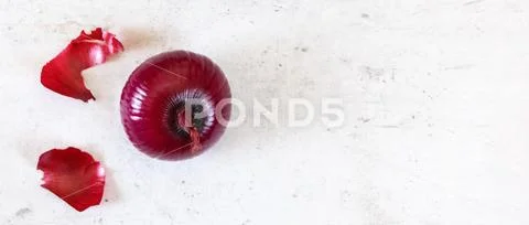 Single red onion, some skin peeled, on stone board, top down view, wide banner Stock Photos