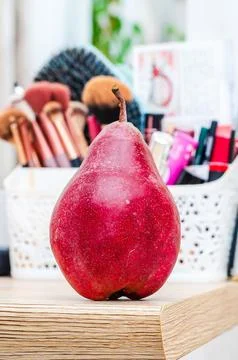 A single red pear sits in front of a collection of makeup brushes and cosmeti Stock Photos