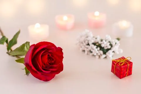 Single red rose, gift box, and candles on white table Stock Photos