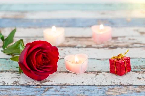 Single red rose, gift box, and candles on vintage table Stock Photos