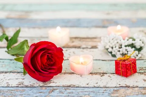 Single red rose, gift box, candles, and white flowers on turquoise table Stock Photos