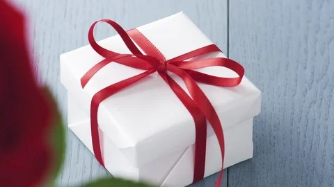 Single red rose in glass with gift box on blue wood table focus pull Stock Footage 100194945