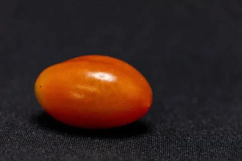 A single, ripe orange grape tomato is photographed up close on a dark backgro Stock Photos
