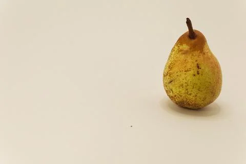 A single ripe pear with a brown stem rests on a light, plain surface, ready f Stock Photos