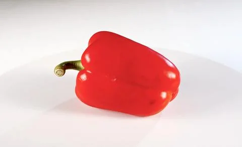 A single, ripe red bell pepper is resting on a white surface Stock-Fotos