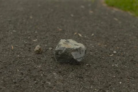 Single rough stone on dark asphalt road surface Stock Photos