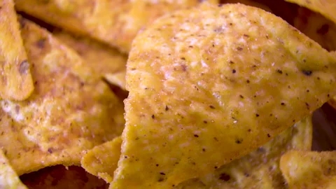 Single seasoned corn nacho chip rotating among a pile, extreme macro Stock Footage 345610830