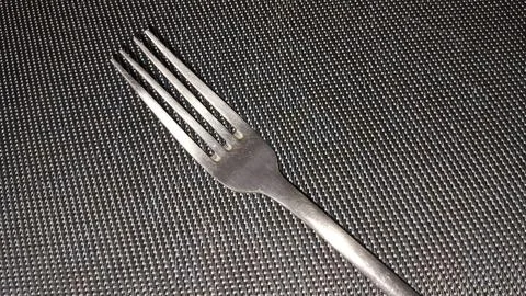 Single silver metal fork resting on a dark woven textured surface Stock Photos