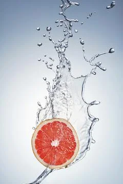 A single slice of fresh red grapefruit being splashed with water. Stock Photos