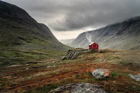 A single small red cabin billows smoke from it's tiny chimney in the remote g Stock Photos