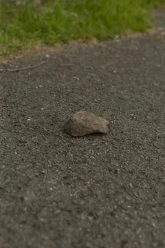 Single small rock on asphalt path with grassy edge Stock Photos