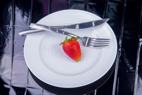 Single strawberry with knife and fork on a white plate Stock Photos