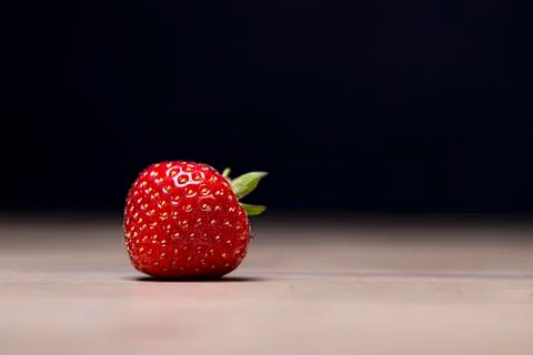 Single strawberry on a table with black background Stock Photos