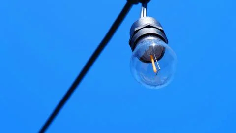 Single string lightbulb hanging against a clear blue sky backdrop. Fotos Stock