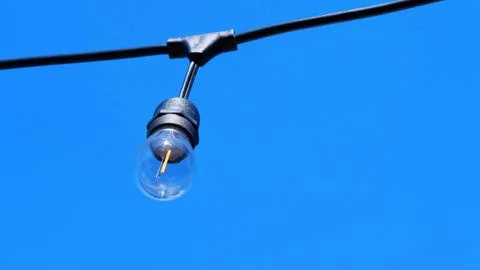 Single string lightbulb hanging against a clear blue sky backdrop. Fotos Stock