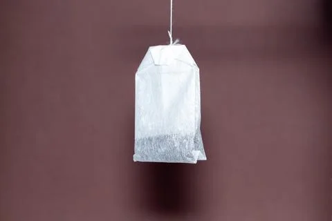 Single tea bag hanging on a string against brown background for beverage Stock Photos