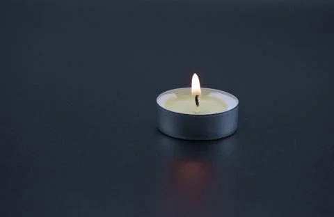 A single tea light burning in an aluminium sleeve on a black background Stock Photos