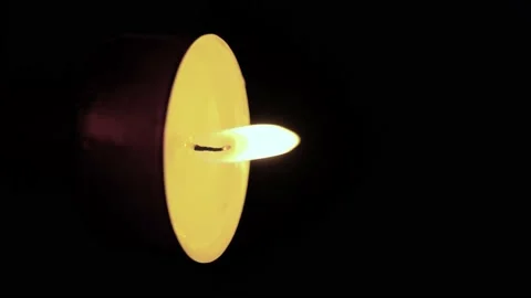 A single tea-light candle lit, in light wind, on a black background. Top copy Stock Footage