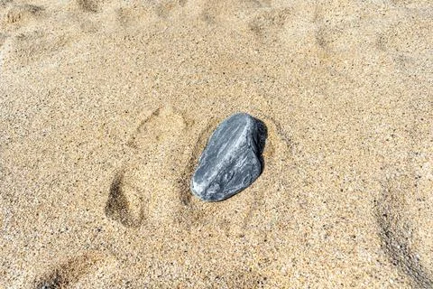 A single textured grey stone isolated on beach sand Stock Photos