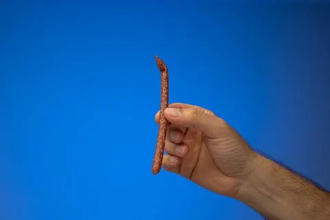 Single thin party snack sausage held in hand by Caucasian male hand. Close up Foto stock