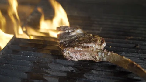 Single tomahawk rib steak on hot black grill with flames underneath. Video stock 117442693
