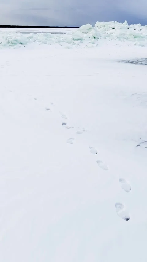 Single trail of footprints across fresh snow toward a pale turquoise pressure Stock Footage 333033087