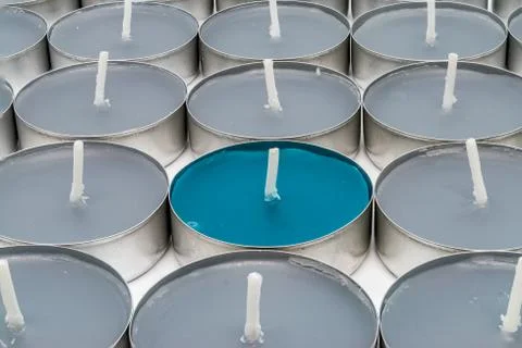 Single turquoise tea candle surrounded by grey ones Stock Photos