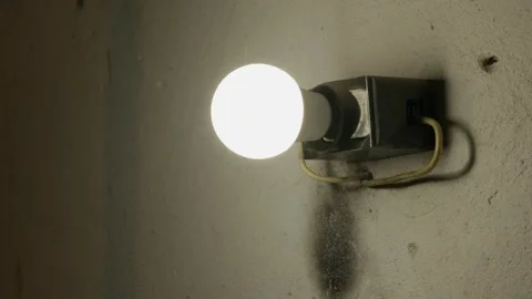 Single Unlit Light Bulb Attached to Wall in Dark Moody Interior 動画素材 335642201