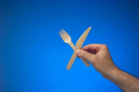 Single use disposable and biodegradable wooden knife and fork held in hand by Fotos de archivo