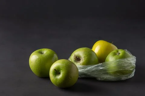 Single use plastic packaging issue. green apples in plastic bags  on a dark b Stock Photos