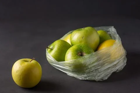 Single use plastic packaging issue. green apples in plastic bags  on a dark b Stock Photos