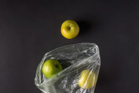 Single use plastic packaging issue. green apples in plastic bags  on a dark b Stock Photos