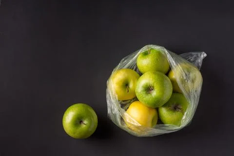 Single use plastic packaging issue. green apples in plastic bags  on a dark b Stock Photos
