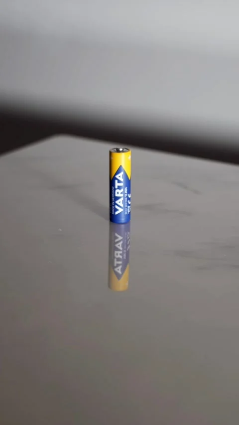 Single Varta AA Battery Standing Upright on a Reflective Marble Table Video stock 325629424