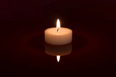 Single white burning tea light with its reflection on a black background Stock Photos