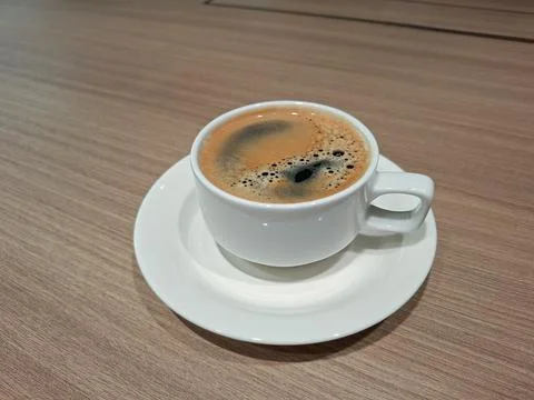 A single white cup of hot coffee with a dark crema pattern sits on a white .. Stock Photos