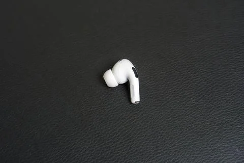 Single white earbud rests on dark textured surface Stock Photos