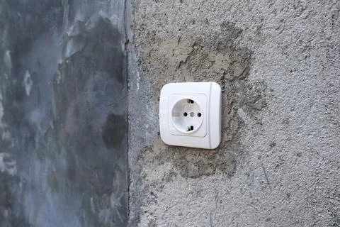 Single white electrical power socket mounted on a rough unfinished concrete.. Stock Photos