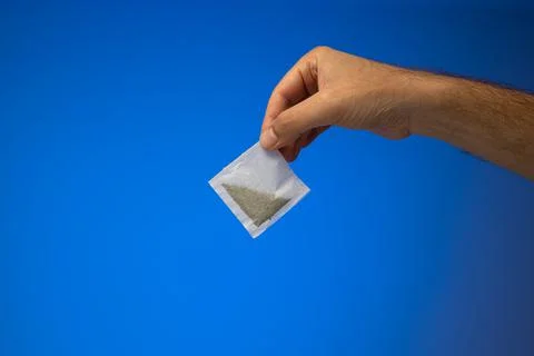 Single white paper tea bag held in hand by Caucasian male hand. Close up stud Foto stock