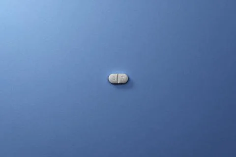 Single white pill on a blue surface Stock Photos
