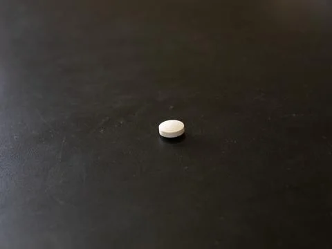Single white round tablet on dark tabletop Stock Photos