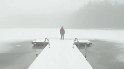 A single woman stands at the end of a long snowy boardwalk over frozen lake Stock Footage 146268853