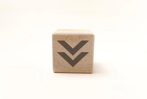 Single wooden block cube featuring a gray downward double-arrow icon on nat.. Stock Photos