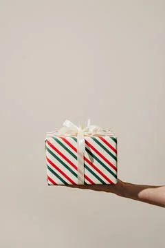 A single wrapped Christmas present with ribbons held in one hand Stock Photos